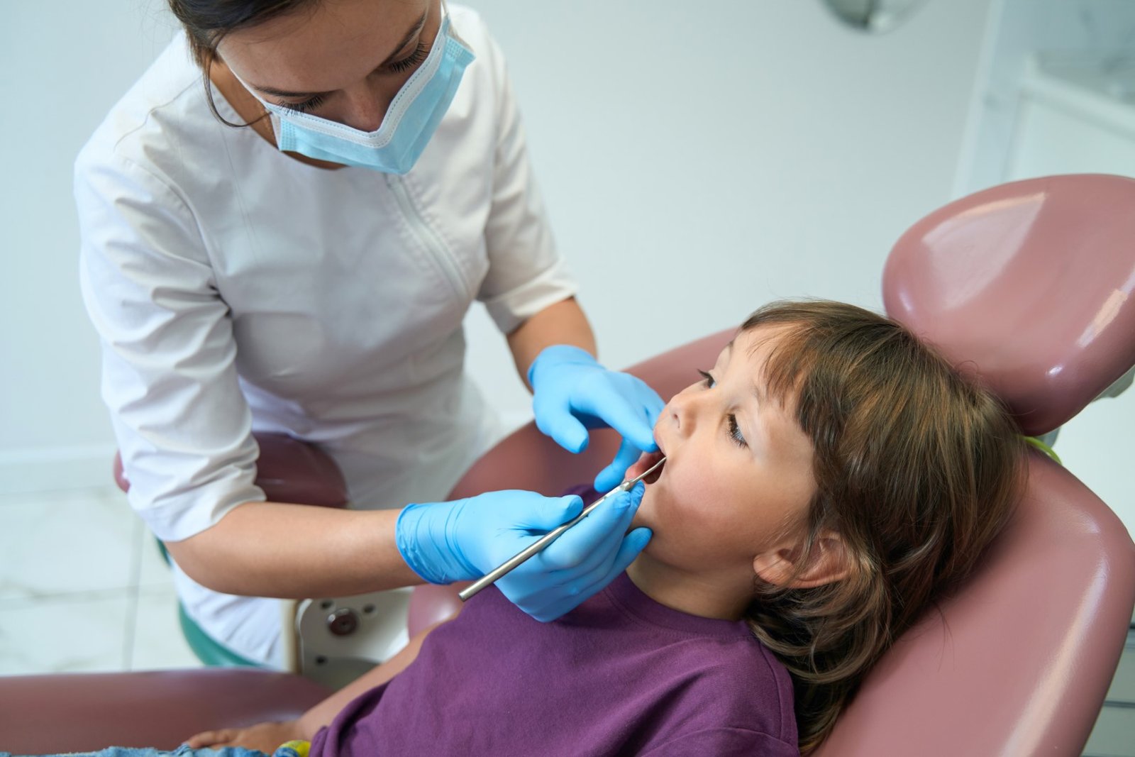 Experienced pedodontist inspecting teeth of little patient